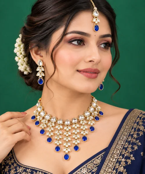 Elegant blue and golden artificial jewellery set featuring a statement necklace with sparkling white stones, rich blue oval stones, and intricate floral detailing.